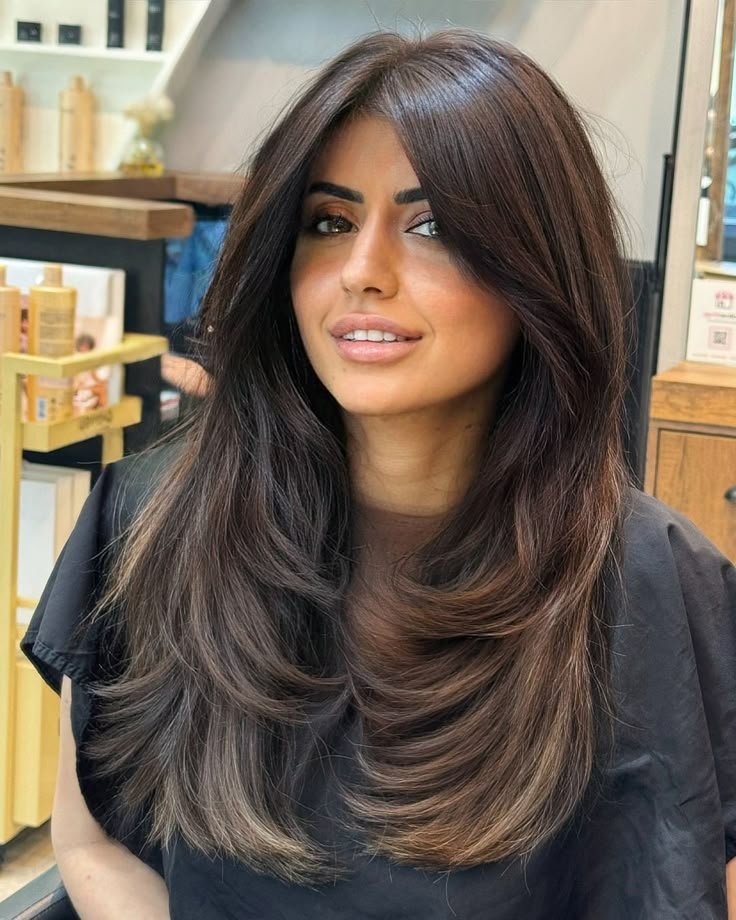 Woman with long, dark brown butterfly haircut featuring voluminous face-framing layers and soft feathered ends.